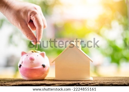 Investor hand hold gold coin save in the piggy bank and home model is destination put on the wood in the public park, Loan and business investment with real estate for future concept.