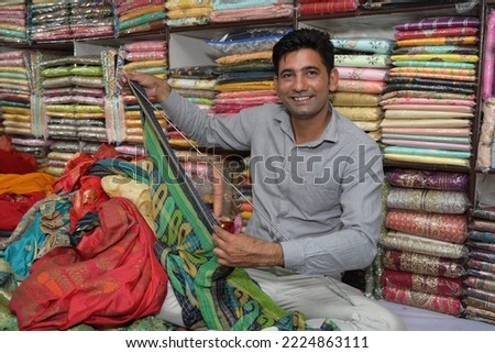An Indian shopkeeper showing clothes from his store Royalty-Free Stock Photo #2224863111