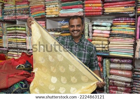 An Indian shopkeeper showing clothes from his store Royalty-Free Stock Photo #2224863121