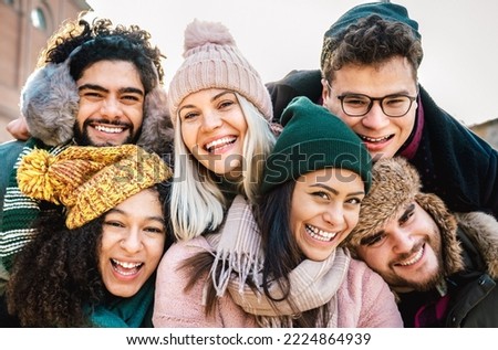 International guys and girls taking funny selfie on warm fashion clothes - Happy life style concept with millenial people having fun together out side on winter holidays - Bright warm filter
