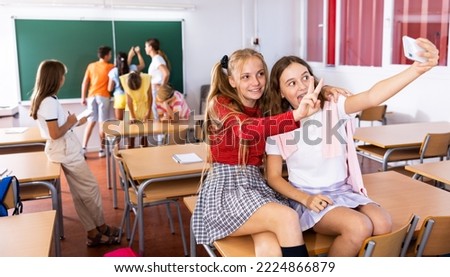 Two cheerful schoolgirls take a selfie during recess in the classroom