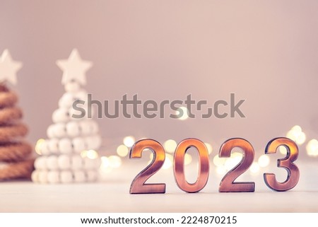 Metal numbers 2023 on a white table with Christmas trees and bokeh lights. Happy New Year 2022 is coming concept.