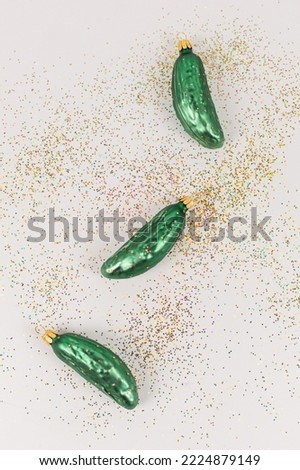 Three Christmas tree baubles in the shape of a cucumber are lying on a white background. Glitter decorate the picture.
