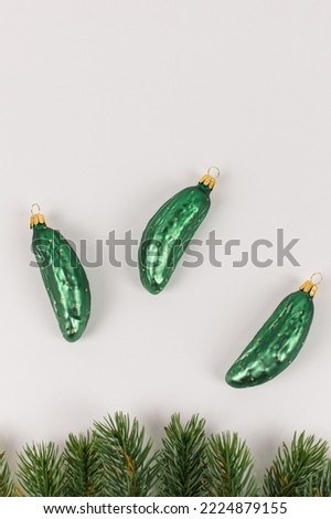 Three Christmas tree baubles in the shape of a cucumber are lying on a white background. Fir branches decorate the picture.