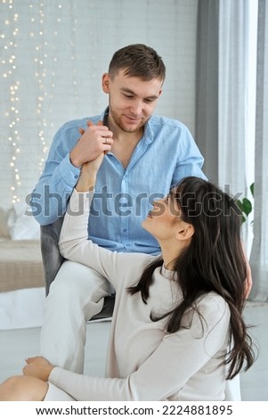 Loving couple near the bed. The girl is sitting on the floor near the bed holding hands with the guy.