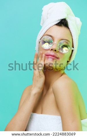 Vertical photo, a woman on a blue background in a towel on her head and body and glasses looks at us