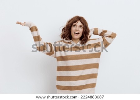 a happy, joyful woman stands on a light background in a striped sweater, smiling happily and raising her hands. Horizontal photo with an empty space for an advertising layout