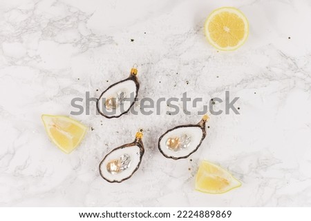 Three Christmas tree baubles in the shape of an oyster are lying on a marble table. Glitter, stars and lemon slices decorate the picture.