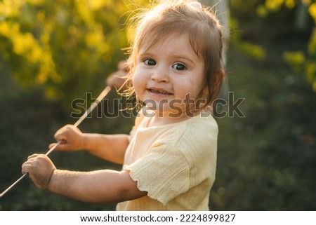 Portrait of little girl smiling while standing in the vines of the garden at the grandmother's house in summer day. Country life, calmness and summer relaxation