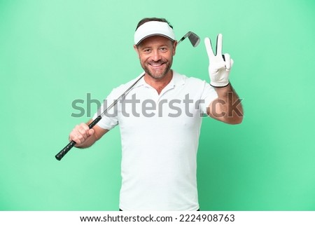 Middle age caucasian man isolated on green background playing golf and and showing victory sign