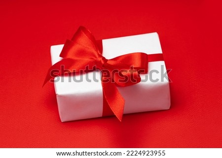 Close up shot of gift box wrapped in white paper and decorated with ribbon bow isolated over bright colored red paper background.
