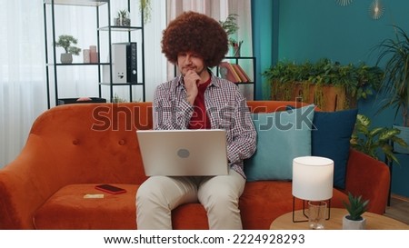 Handsome adult man freelancer at home living room sitting on orange couch, opens laptop start working. Young guy works on notebook, sends messages, makes online purchases, watching movies, working