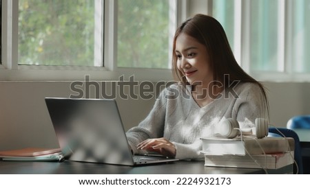 Happy young Asian student girl using laptop in university campus or at virtual office. College female student learning remotely.