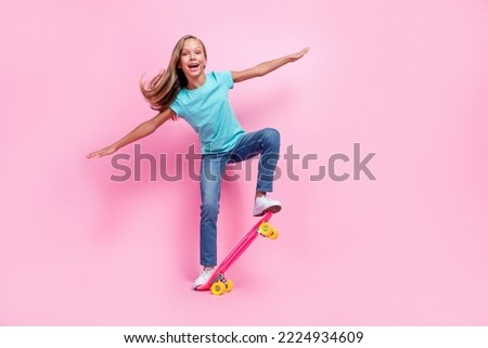 Full length photo of sweet excited small kid wear turquoise t-shirt riding skateboard empty space isolated pink color background