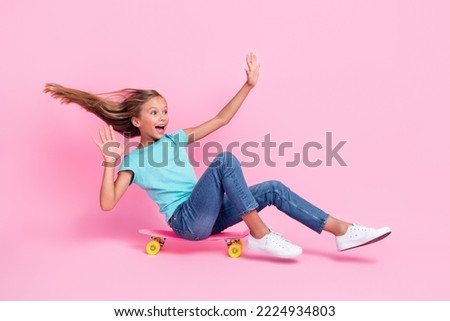 Full length photo of pretty impressed small kid wear turquoise t-shirt riding skateboard looking empty space isolated pink color background
