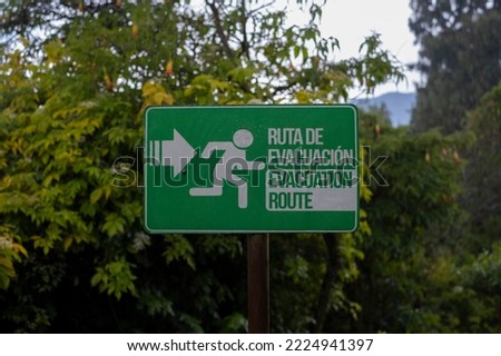 Sign in Spanish and English evacuation route with a direction arrow pointing to the right posted in the rain forest, shot during heavy rain. Safety, danger, natural disaster concept.