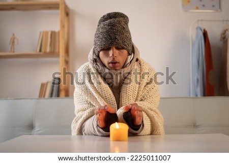 Tired man who warm hands over candlelight at home no heating. Shutdown of heating and electricity, power outage, blackout, load shedding or energy crisis Royalty-Free Stock Photo #2225011007