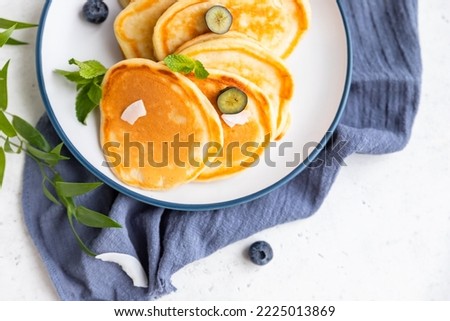 Traditional fluffy pancakes with orange jam, blueberries, coconut chips and mint for healthy breakfast, light grey background. High key photography.
