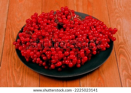 Red viburnum berry, cranberry.In a black plate. Still life on a wooden background.Fruit composition.Close-up. place for text