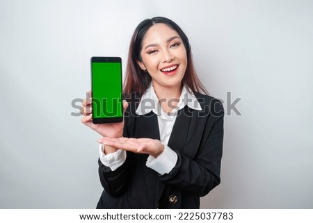 A happy young businesswoman is wearing black suit, showing copy space on her phone isolated by white background