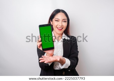 A happy young businesswoman is wearing black suit, showing copy space on her phone isolated by white background