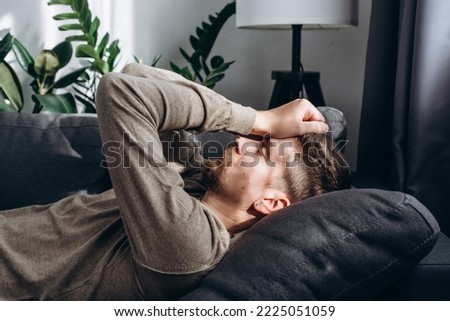 Young handsome ill sick man lying alone on couch at home, suffering from headache, Illness, loneliness, boring life concept. Close up portrait of tired lonely exhausted overworked bored guy