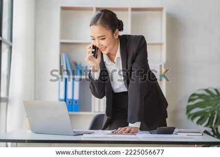 Young beautiful asian woman using smartphone and working with laptop while sitting at office desk, working from home concept.