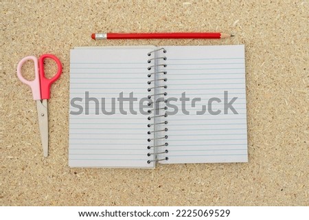 blank lined note pad with a pencil and small paper scissors on a wooden background
