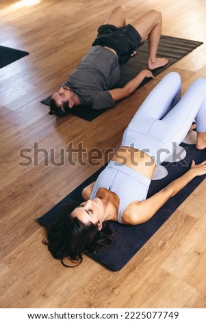 High angle view of young people doing the glute bridge exercise while lying on fitness mats in a yoga studio. Sporty man and woman practicing hatha yoga in an exercise class. Royalty-Free Stock Photo #2225077749