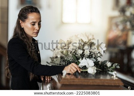 Funeral, sad and woman with flower on coffin after loss of a loved one, family or friend. Grief, death and young female putting a rose on casket in church with sadness, depression and mourning Royalty-Free Stock Photo #2225083801