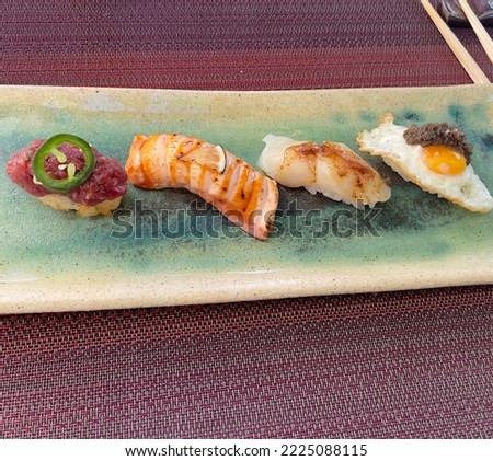 Picture portraying original japanese sushi creations served in Kabuki restaurant in Madrid. 4 Nigiri consisting of  egg, flambeed salmon, Toro and roasted scallop