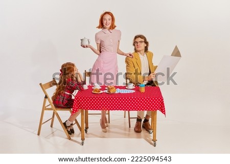 Portrait of beautiful young family having breakfast together isolated on grey background. Movie remake. Housewife. Beauty, retro style, fashion, elegance, 60s, 70s, family concept. Copy space for ad Royalty-Free Stock Photo #2225094543