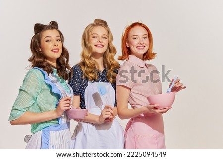 Portrait of beautiful young women, housewives with cooking tools isolated over grey background. Pop art. Concept of beauty, retro style, fashion, elegance, 60s, 70s, family. Copy space for ad Royalty-Free Stock Photo #2225094549