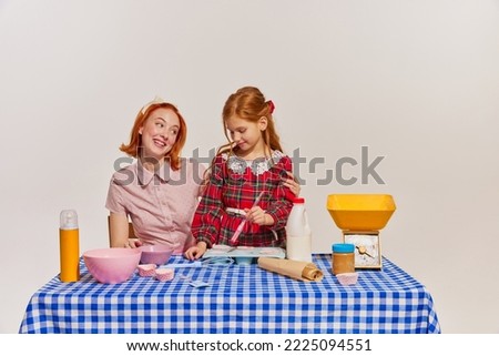 Portrait of mother and daughter cooking cake together isolated over grey background. Hobby for girls. Concept of beauty, retro style, fashion, elegance, 60s, 70s, family. Copy space for ad Royalty-Free Stock Photo #2225094551