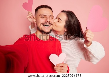 Portrait of lovely young couple, woman kissing happy and smiling man, taking selfie together isolated over pink background. Concept of love, relationship, Valentine's Day, emotions, lifestyle Royalty-Free Stock Photo #2225096175