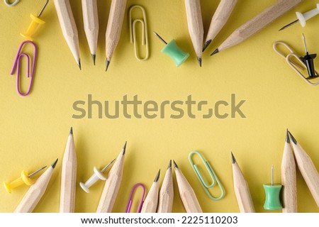 Pencils and colored paper clips lies on a yellow background. Education concept with copy space for text. Flat lay of pencils, paper clips on pastel office desk. Minimalistic close-up macro photography