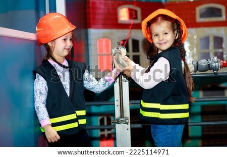 Two little girls dressed as firefighters play role-playing games and water a toy house with a hose, girls in a hard hat, children's games.
 Royalty-Free Stock Photo #2225114971