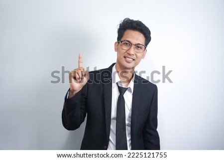 Attractive young Asian man in suit pointing up with his finger isolated on white background