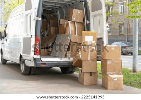 Open lorry car trunk with moving cardboard packages outdoors. White delivery van and many different cardboard boxes at city street. Royalty-Free Stock Photo #2225141995