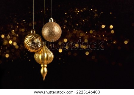 Christmas card with three golden balls decorations on black background with bokeh lights