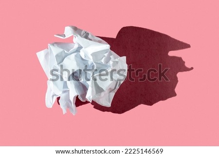 Crumpled white paper sheet in form of ball on a pink background with hard light
