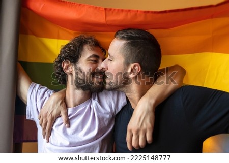 Passionate gay couple making out with lgbtq flag in the background. Young gay couple bonding fondly indoors.
