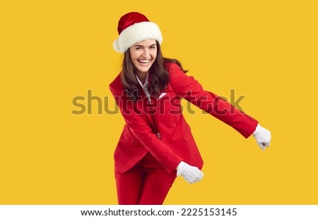 Laughing cheerful young brunette woman wearing Santa style red suit and Xmas hat, white gloves dancing swish swish backpack shuffle dance on yellow background. Christmas, Xmas, New Year banner.