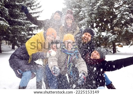 Group of happy millennial friends having fun in the snow. Bunch of cheerful adult people in warm hats, coats and jackets throwing snow in the air for a funny group photo in a winter forest