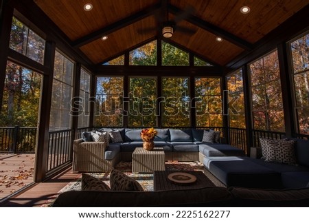 Cozy screened porch enclosure with contemporary furniture at Thanksgiving Holiday. Porch door open, flower bouquet in a vase, autumn leaves and woods in the background.