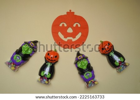 Cute character in monster costume. Scary Halloween figurines stand on a light background in close-up, behind hangs terrible pumpkin. Halloween concept. Holiday decorations, toys
