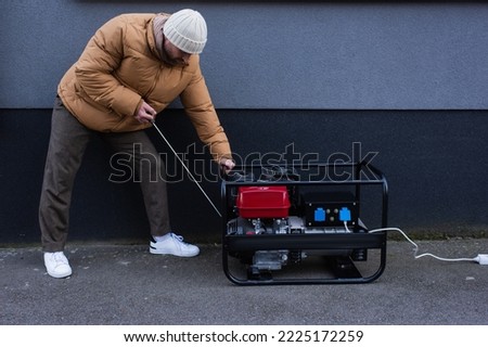 man in down jacket starting power generator during electricity shutdown Royalty-Free Stock Photo #2225172259