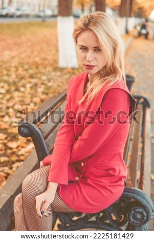 Portrait of a blonde next to a red-orange bush in autumn. The concept of the autumn season.