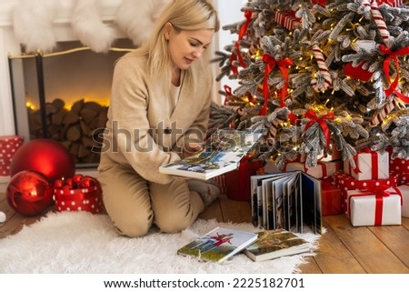 Beautiful young woman is looking her old photo album while spending Christmas alone at home