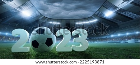 Poster with soccer ball lying on grass of football field between huge numbers 2023 in crowded stadium with spotlight in evening. Concept of sport, energy, power. Flyer for ad, design